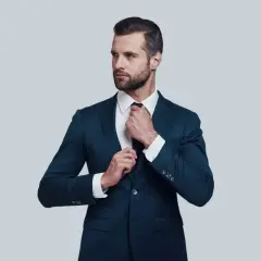 Elegancki mężczyzna w granatowym garniturze i białej koszuli poprawia krawat. Idealna stylizacja, gdy zastanawiasz się, jaka koszula do granatowego garnituru.
