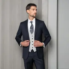 Elegancki mężczyzna w granatowym garniturze i jasnej kamizelce, z niebieskim wzorem na krawacie.