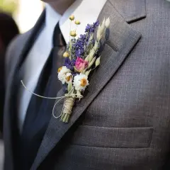 Elegancka, szara marynarka z czarnym krawatem i delikatną, suszoną butonierką z lawendą i białymi kwiatkami.
