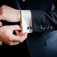 Mężczyzna zapina mankiety koszuli, przygotowując się do ważnego wydarzenia. Eleganckie spinki dodają stylu.