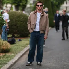 Mężczyzna w beżowej kurtce i szerokich jeansach, zastanawia się jakie buty do szerokich spodni będą najlepsze.