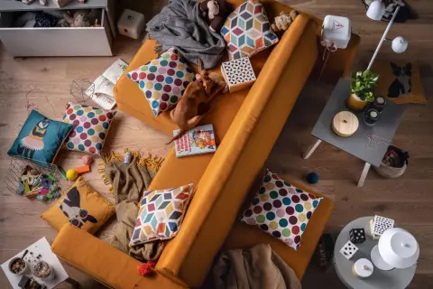 Kanapa w kolorze musztardowym, na niej piesek i poduszki. Jaki kolor pasuje do pomarańczowego? Zobacz, jak świetnie komponują się z nią wielokolorowe wzory!