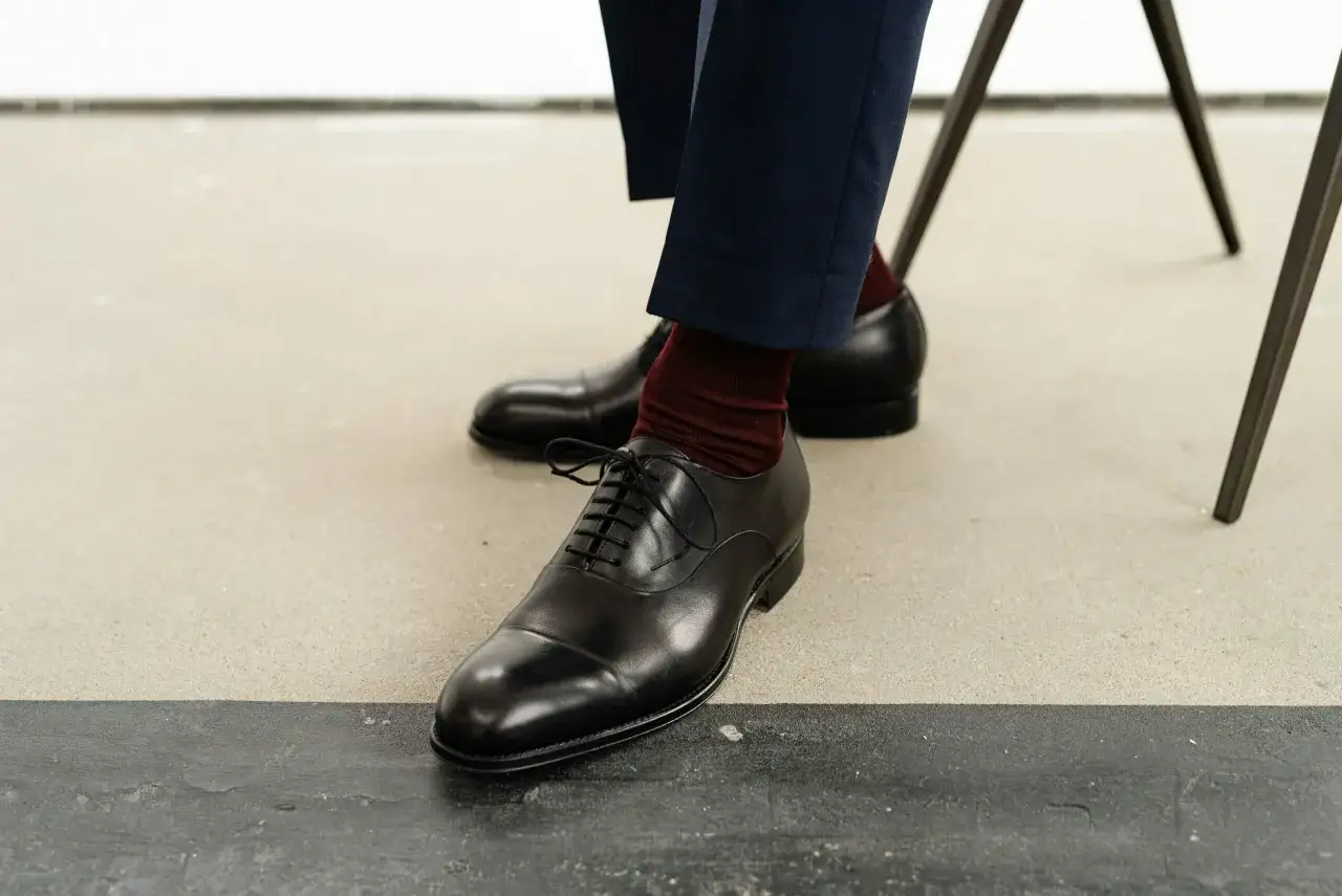 Eleganckie, czarne eskarpiny z bordowymi skarpetkami i granatowymi spodniami.