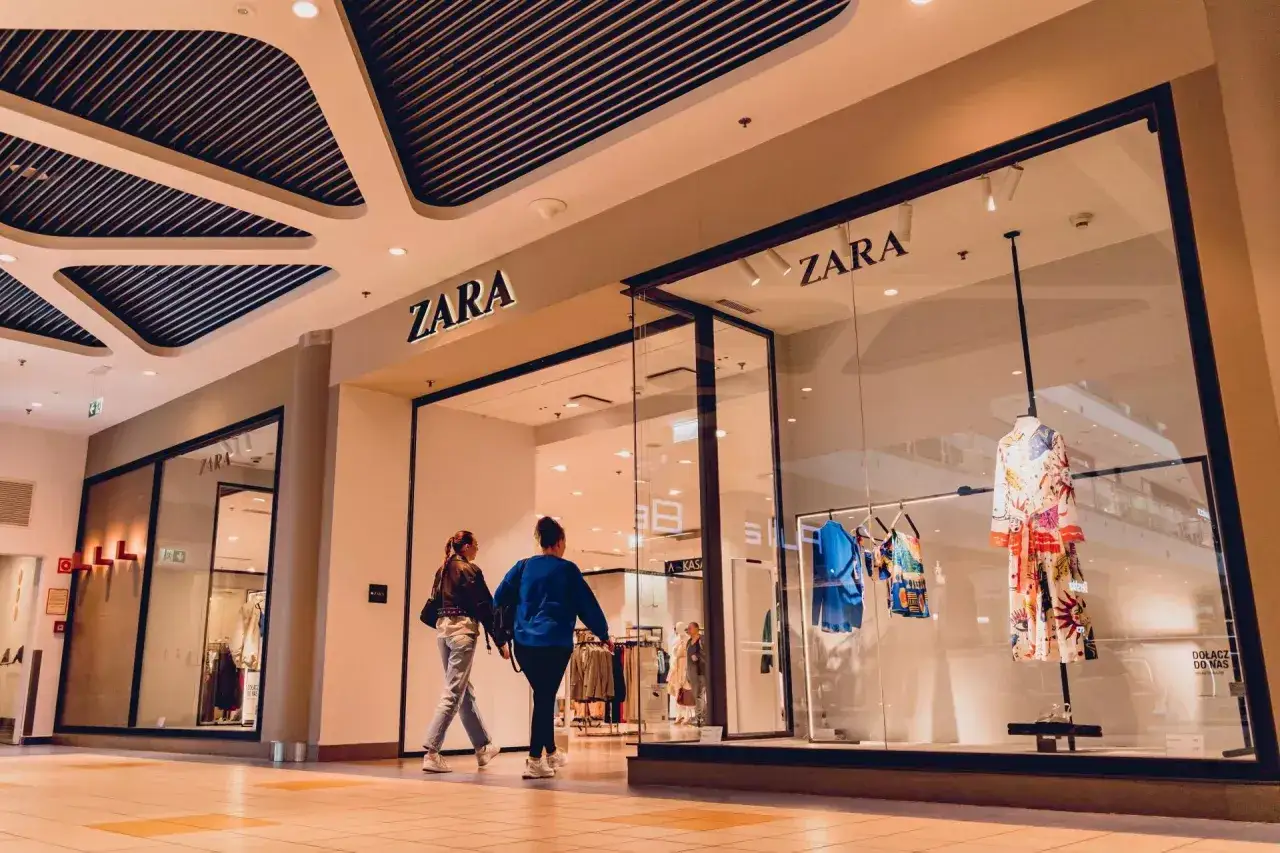 Dwie kobiety wchodzą do sklepu ZARA, części imperium Inditex. W witrynie wisi kolorowa sukienka.